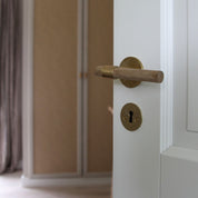 SIGNATURE door handle in Brushed Brass/Oak. Modern door hardware made of solid brass by BRANDT Collective.